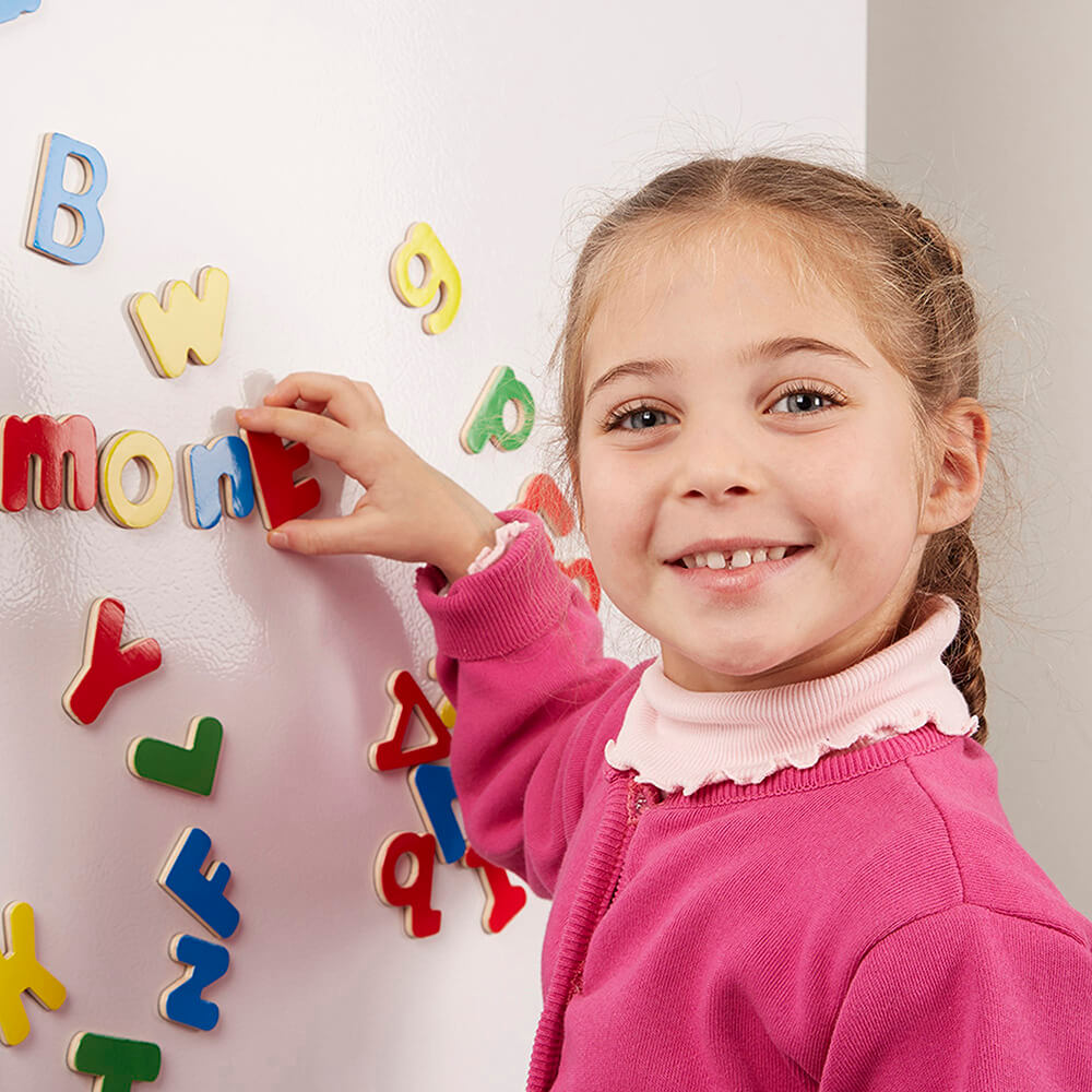 Girl playing with the Melissa and Doug Wooden Letter Alphabet Magnets on the wall